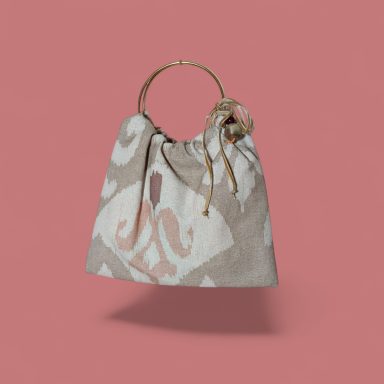 Raíces Rosadas Bolso de tela beige con diseño abstracto y asa dorada, sobre fondo rosa.